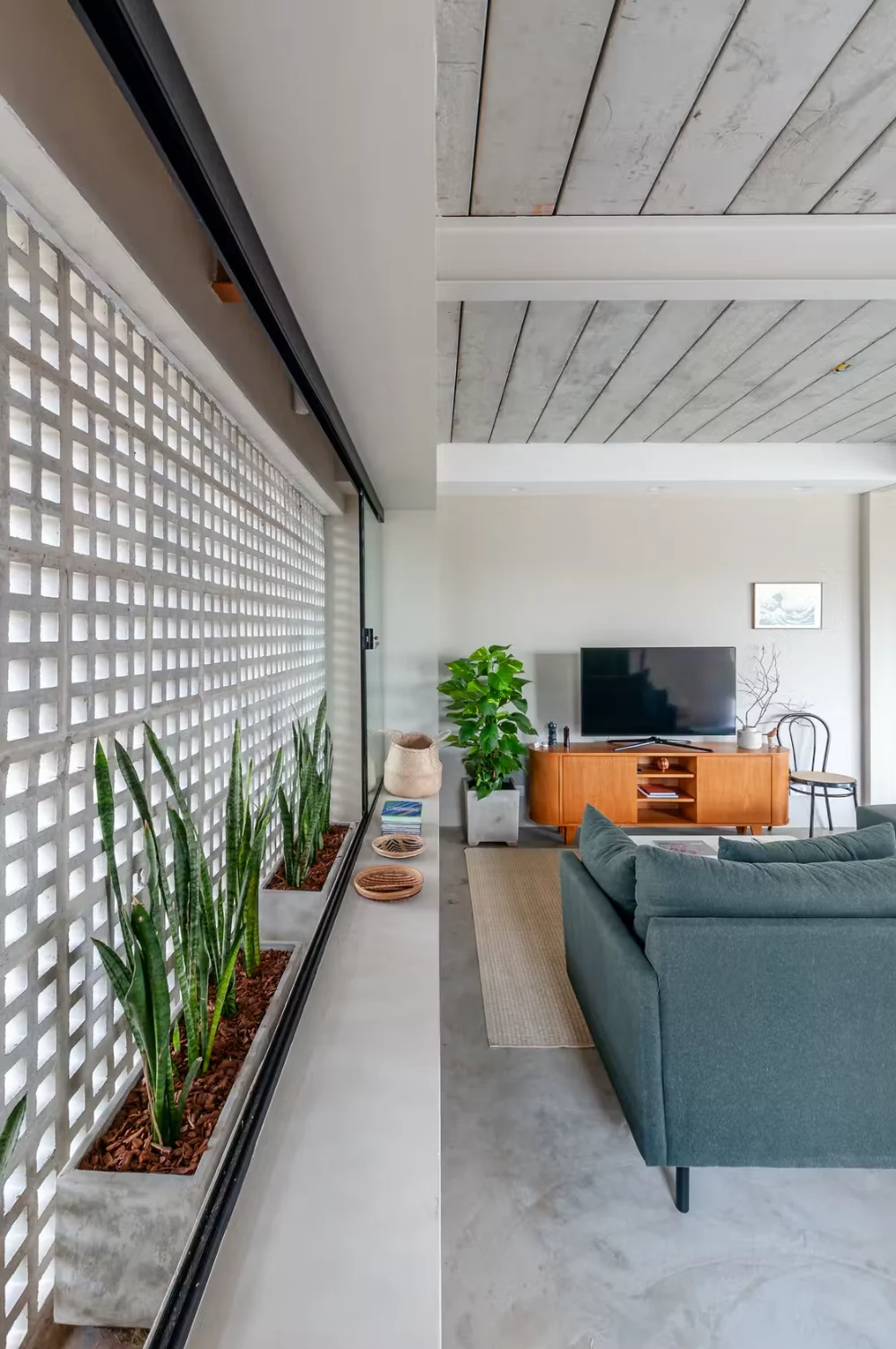 Sala de estar com painel de cobogó branco de concreto e plantas, banhada por luz natural